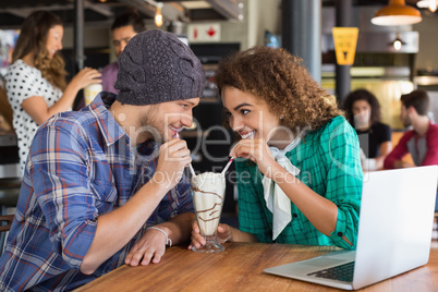 Happy couple looking at each other while having milkshake