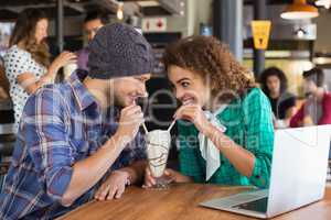 Happy couple looking at each other while having milkshake