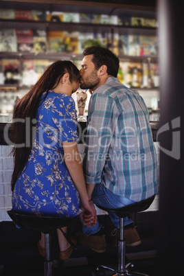 Affectionate man holding hands while kissing woman at counter