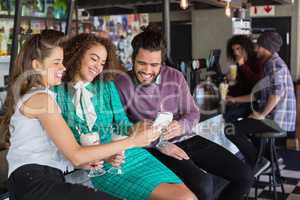 Friends discussing over mobile while having drink in restaurant