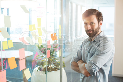 Portrait of young businessman with arms crossed standing at office