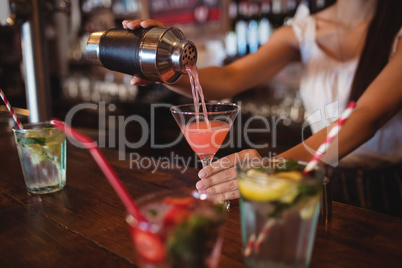 Mid section of female bartender pouring cocktail drink in the glass