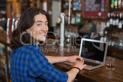 Smiling young man using laptop at bar counter