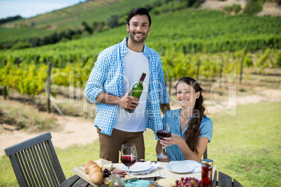 Portrait of smiling couple holding red wine bottle and glass