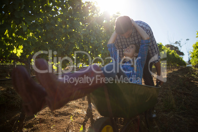 Young man pushing his happy girlfriend in wheelbarrow at vineyard