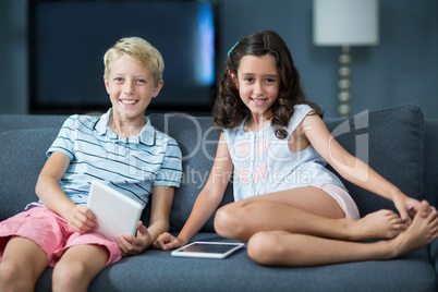 Happy siblings sitting on sofa with digital tablet in living room