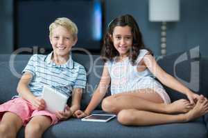 Happy siblings sitting on sofa with digital tablet in living room