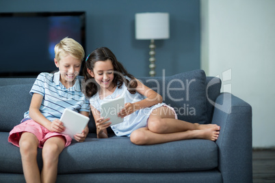 Happy siblings sitting on sofa and using digital tablet in living room