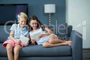 Happy siblings sitting on sofa and using digital tablet in living room