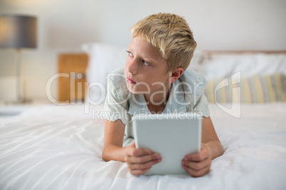 Thoughtful boy with digital tablet lying on bed