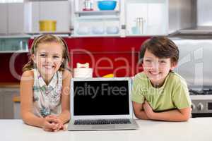 Smiling siblings with laptop on worktop in kitchen
