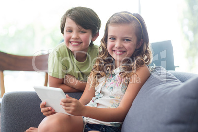 Portrait of siblings with digital tablet sitting on sofa in living room