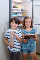 Siblings holding cake and bottle in kitchen
