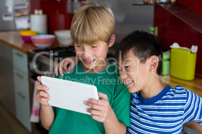 Siblings using digital tablet in kitchen