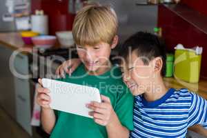 Siblings using digital tablet in kitchen