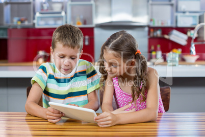 Siblings using digital tablet in kitchen