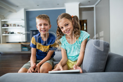 Portrait of siblings with digital tablet sitting on sofa in living room