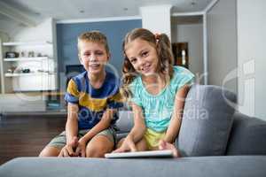 Portrait of siblings with digital tablet sitting on sofa in living room