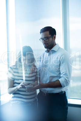 Business couple using mobile phone by glass window