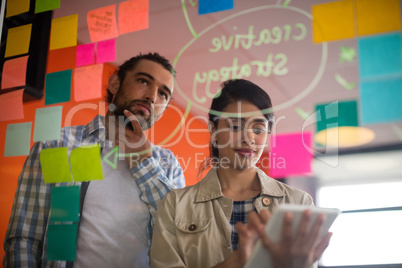 Female executive using digital tablet while male executive looking at sticky notes