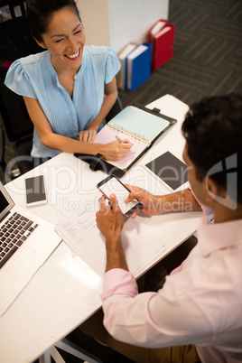 Smiling businesswoman discussing with male colleague at desk