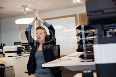 Businesswoman practicing yoga while sitting on chair by desk