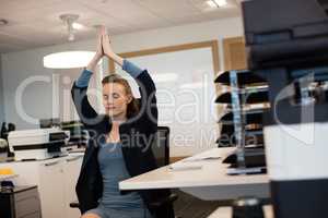 Businesswoman practicing yoga while sitting on chair by desk