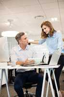 Businessman discussing with female colleague while sitting at desk