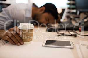 Businessman sleeping while holding disposable coffee up on desk