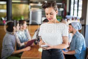 Beautiful waitress standing by customers in restaurant