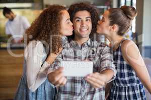 Portrait of young man taking selfie with female friends in cafe