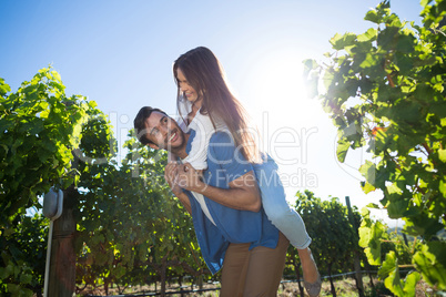 Happy young couple piggybacking against sky at vineyard