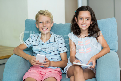 Smiling siblings using digital tablet and mobile phone in living room