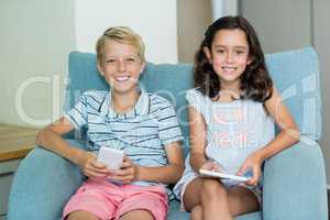 Smiling siblings using digital tablet and mobile phone in living room