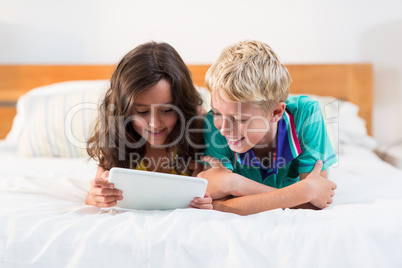 Smiling siblings using digital tablet on bed in bedroom