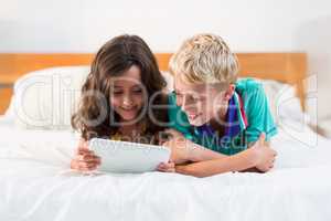 Smiling siblings using digital tablet on bed in bedroom