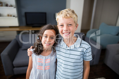 Siblings standing with arm around in living room