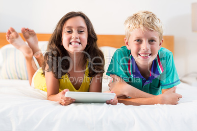 Portrait of smiling siblings with digital tablet lying on bed