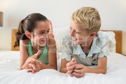 Smiling siblings lying on bed in bedroom