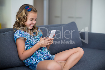 Happy girl sitting on sofa and using mobile phone in living room