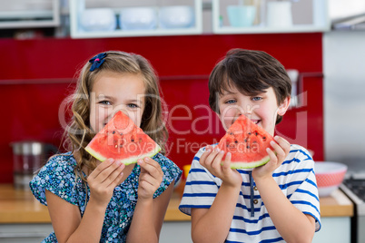 Smiling siblings having watermelon in kitchen