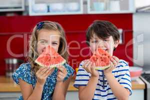 Smiling siblings having watermelon in kitchen