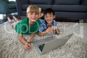 Portrait of smiling siblings with laptop lying on rug