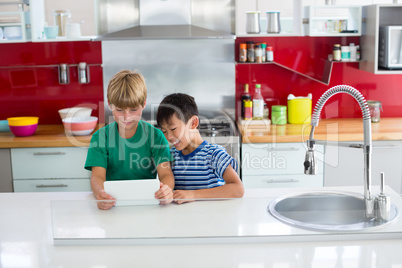 Siblings using digital tablet in kitchen