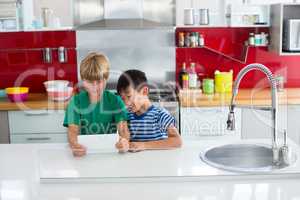 Siblings using digital tablet in kitchen