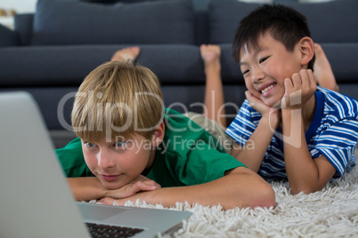 Smiling siblings lying on rug and using laptop in living room