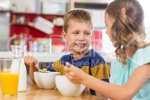 Smiling sibling having breakfast cereal in kitchen