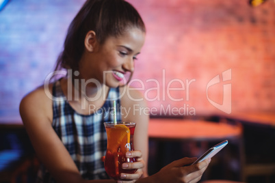 Young woman using mobile phone while having cocktail drink