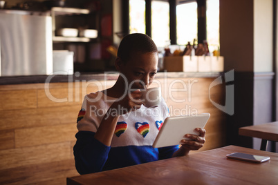 Woman using digital tablet while drinking coffee