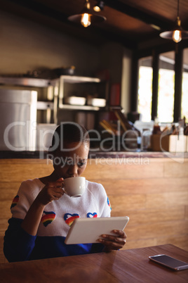 Woman using digital tablet while drinking coffee